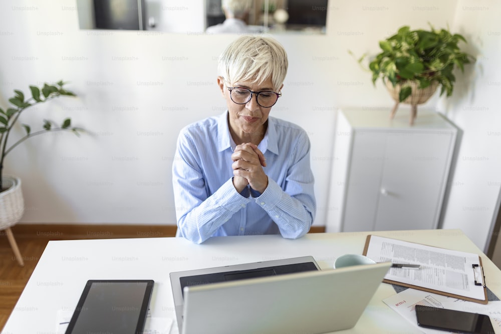Portrait of casual woman using her laptop while sitting home office and working. An attractive middle aged businesswoman sitting in front of laptop and managing her small business from home.