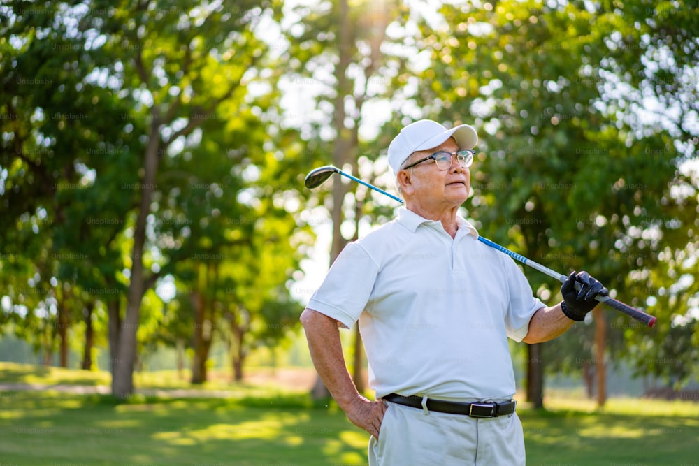 여름 화창한 날에 골프 코스에 서서 골프 클럽을 들고 웃고 있는 아시아 노인 골퍼의 초상화. 건강한 노인 남성은 골프 컨트리 클럽에서 야외 라이프 스타일 활동 스포츠 골프를 즐깁니다.