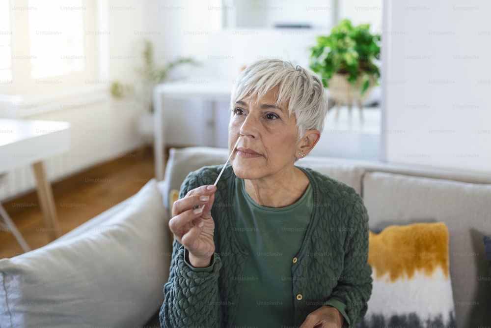 Mature woman taking a Self-swabbing home tests for COVID-19 at home with Antigen kit. Introducing nasal stick to check the infection of Coronavirus. Quarantine, pandemic.