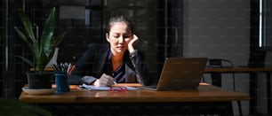 Tired young businesswoman sitting at her office desk with laptop computer.