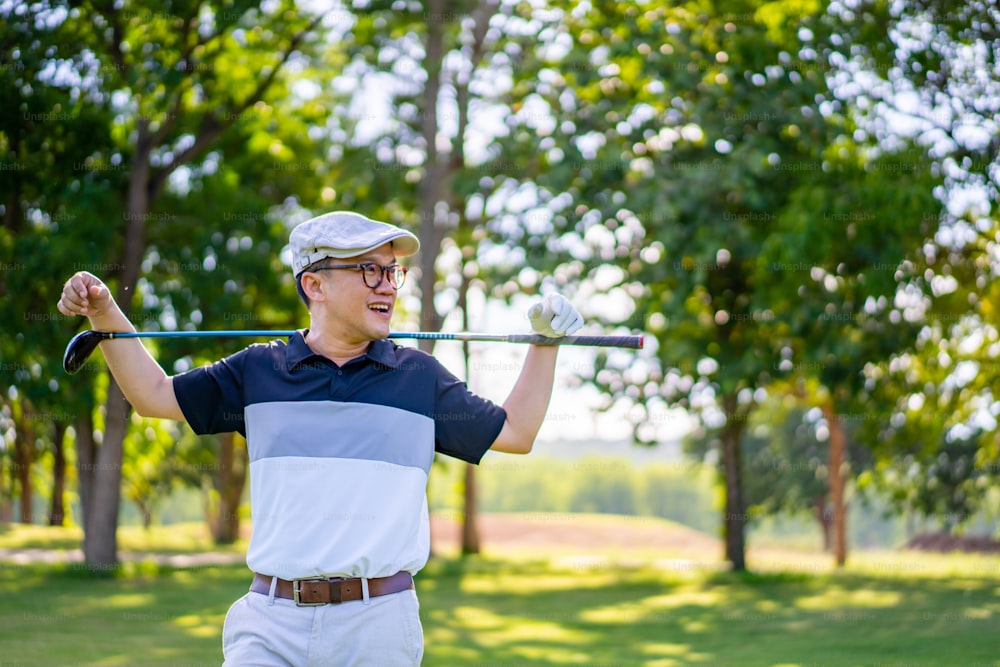 Porträt eines lächelnden asiatischen Mannes, der den Golfschläger hält, der an sonnigen Tagen auf dem Fairway des Golfplatzes steht. Gesunder männlicher Golfer genießt Outdoor-Lifestyle-Aktivität Sport Golf im Country Club im Sommerurlaub