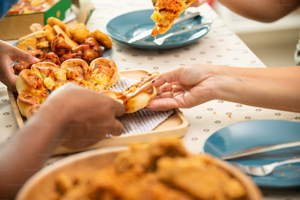 Happy African family parents and two little daughter eating fried chicken and pizza for dinner together. Father and mother and cute child girl kid enjoy and fun eating and sharing a meal together at home