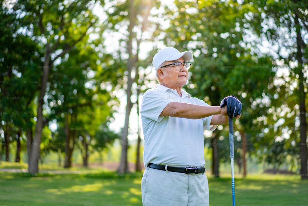 Retrato do golfista sênior asiático sorridente segurando o taco de golfe em pé no campo de golfe no dia ensolarado do verão. Homens idosos saudáveis desfrutam de atividade de estilo de vida ao ar livre esporte golfe no clube de campo de golfe.