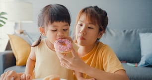 Happy Asia family mom and toddler girl eating donuts and having fun relax enjoy on couch in living room at house. Spending time together, Social distance, Quarantine for coronavirus.