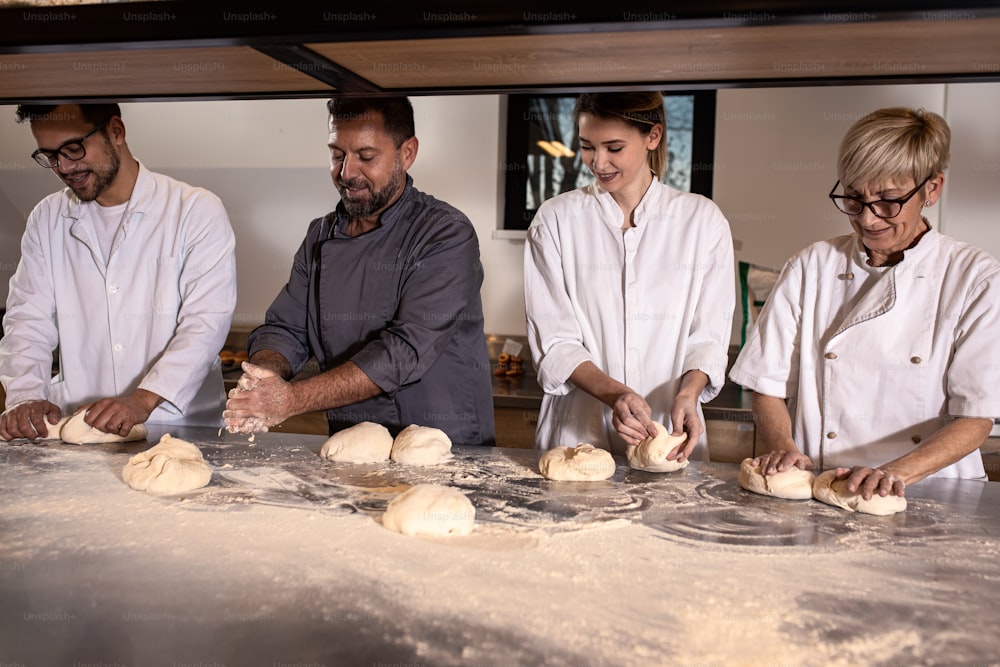 Group of bakers in uniform preparing dough for bread in modern manufacturing.