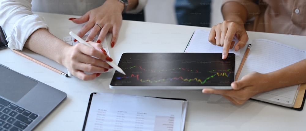 Immagine ritagliata di due donne d'affari che analizzano insieme il grafico finanziario sulla tavoletta digitale.