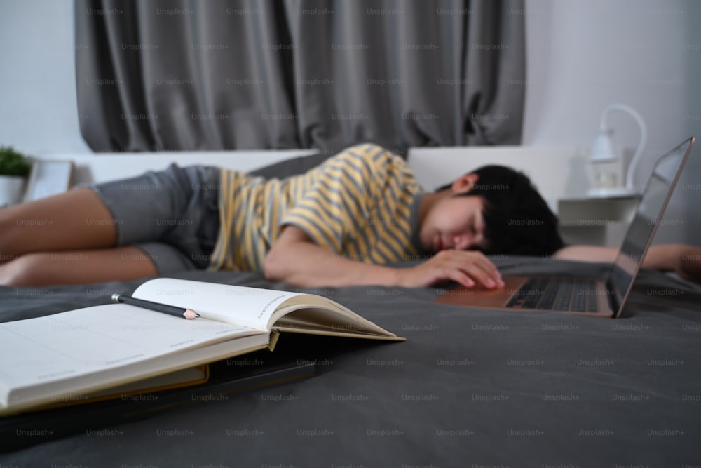 ラップトップでベッドで寝ている疲れたアジア人男性。