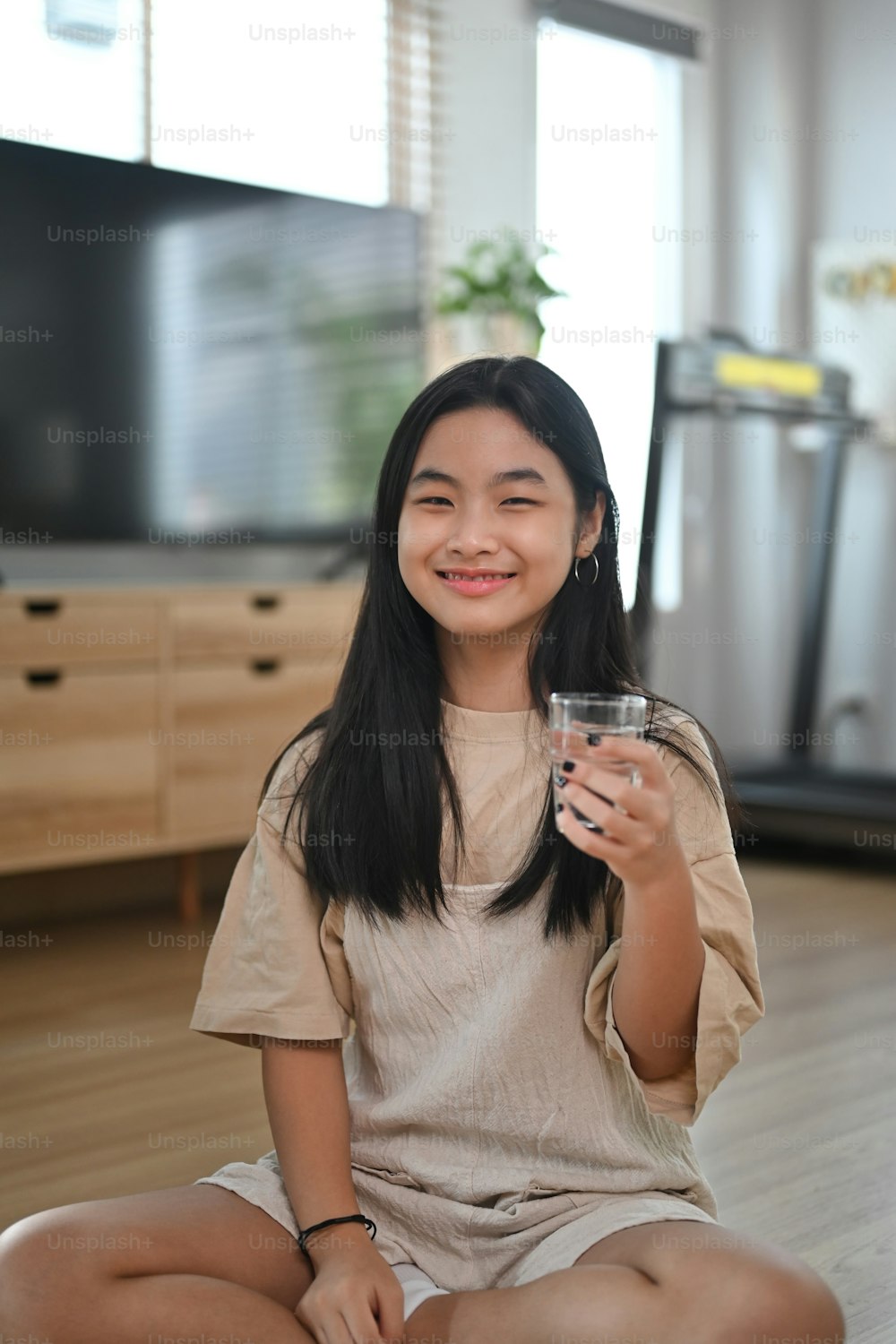 Portrait of cheerful asian girl holding glass of water and smiling to camera. Healthy Lifestyle concept.