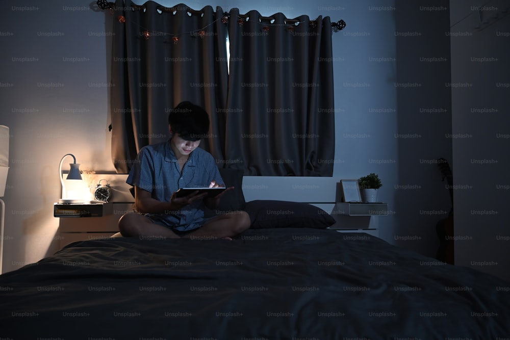 Night shot of young man surfing internet with digital tablet in his bed.