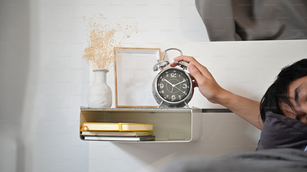 Man lying in bed and hand reaching to turn off alarm clock switch.