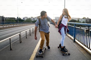 Portrait of happy couple having fun while driving a long board in city outdoors. People skateboard concept