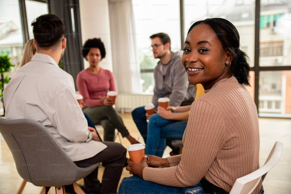 Portrait of a woman with diverse group of people sitting in circle in group therapy session.