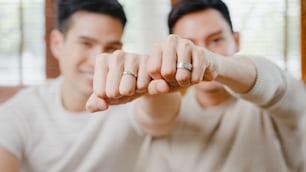 Portrait Young Asia Gay couple feeling happy showing ring at home. Asia LGBTQ+ men relax toothy smile looking to camera while hug in modern living room at house in the morning concept.