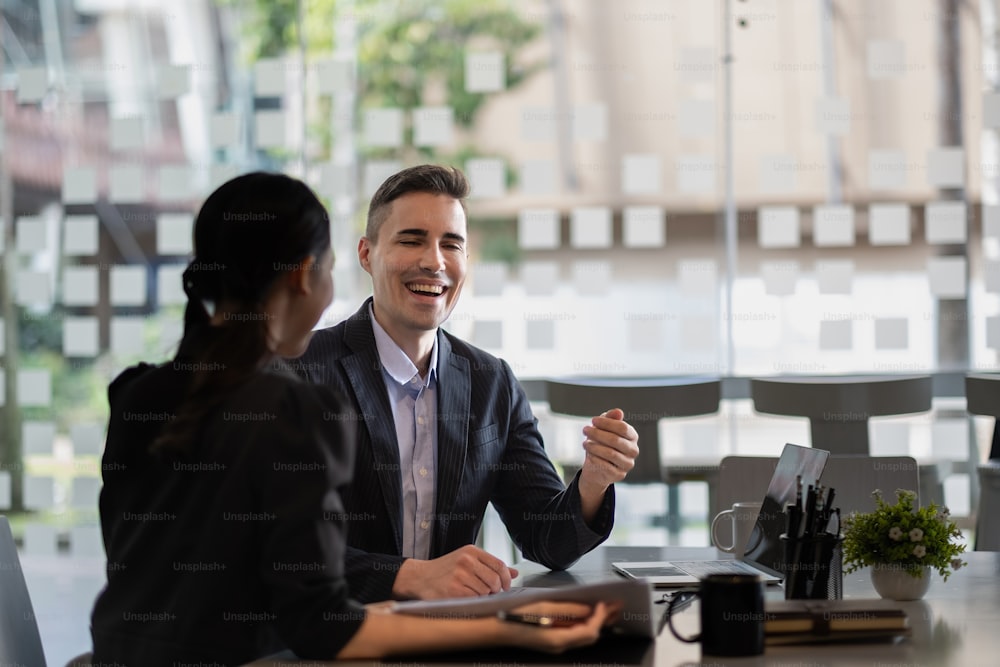 Asian and caucasian businesspeople learn new business app, apprentice listen associate tell about corporate program. Multiracial client and bank manager at business meeting using laptop negotiating.