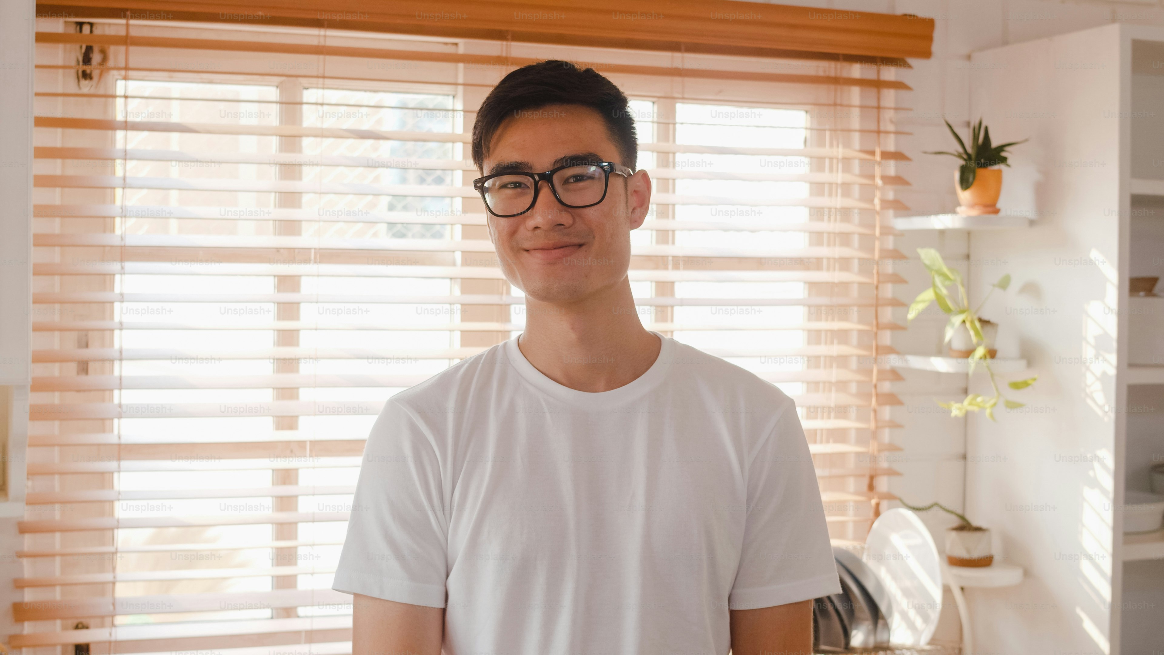 Happy young Asian male feeling happy smiling and looking to camera while relax in kitchen at home.
