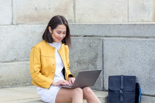 Beautiful asian woman using laptop computer. Smiling asian girl sitting on stairs and using a laptop. Asian business woman using laptop computer