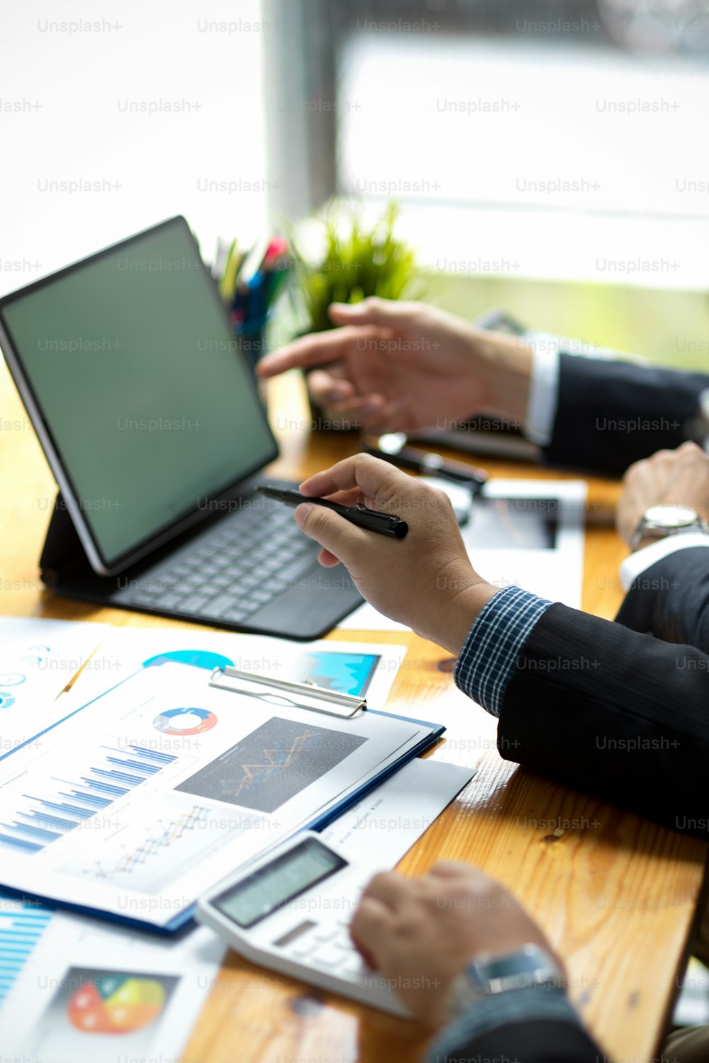 Cropped and focused image of a businessman's hands holding a pen and pointing at a tablet touchpad screen on a desk.