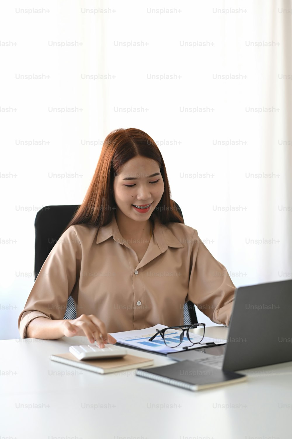 Portrait of smiling businesswoman sitting in modern workplace an working with laptop.