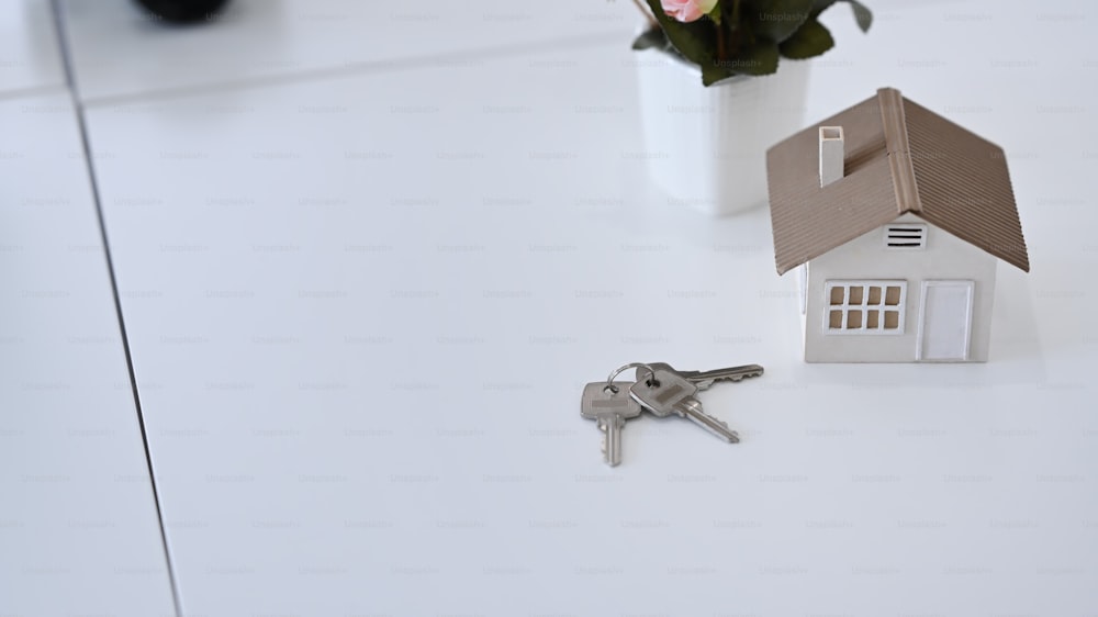 Piccolo modello di casa e chiavi su tavolo bianco. Concetto di investimento ipotecario e immobiliare.