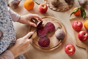 Woman cutting red beet root - preparation for juicing fresh fruits and vegetables