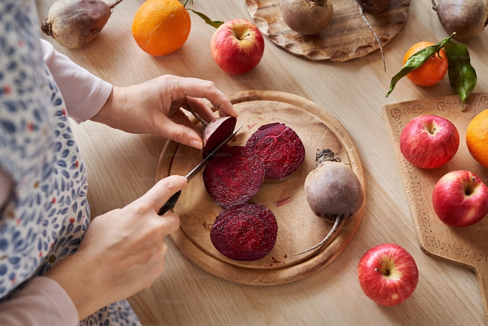 Mujer cortando raíz de remolacha roja: preparación para exprimir frutas y verduras frescas