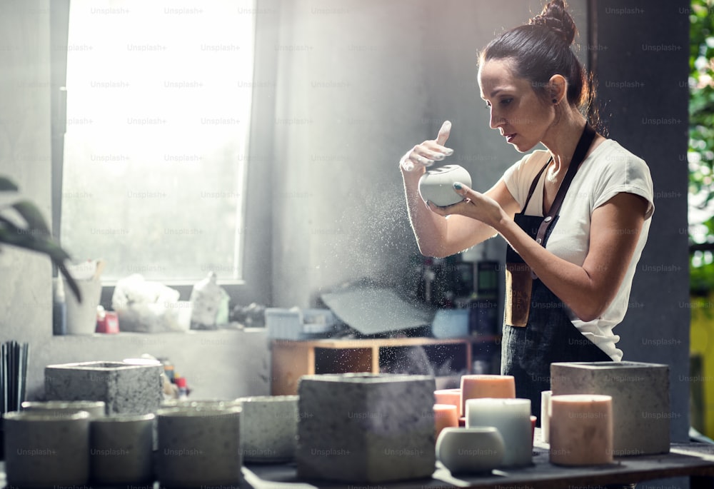 Craftswoman in apron working in her workshop making decorative concrete vase.
