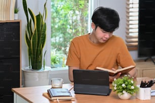 Asian man sitting in living room and reading book.