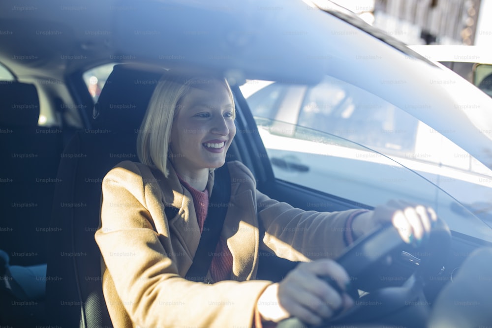Happy blond woman driving a car. Portrait of beautiful caucasian woman with toothy smile driving car. Hand on steering wheel. Young woman driving a car in the city