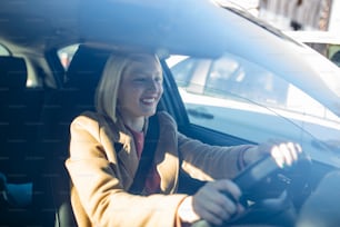 Happy blond woman driving a car. Portrait of beautiful caucasian woman with toothy smile driving car. Hand on steering wheel. Young woman driving a car in the city