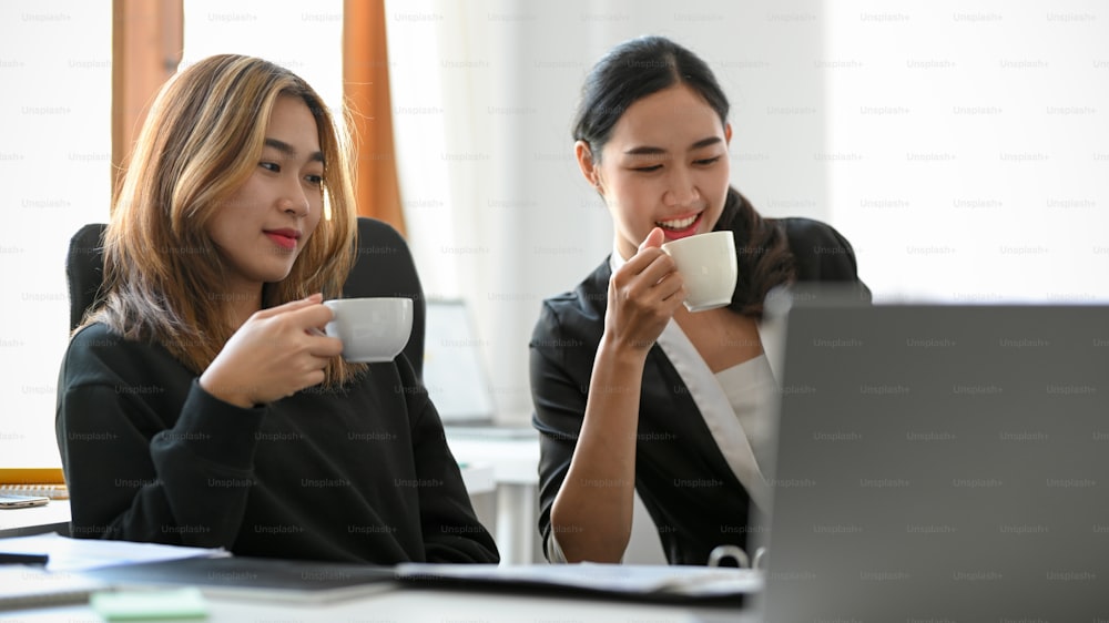 Due manager asiatiche stanno bevendo un caffè caldo durante una riunione e discutono di business plan in ufficio.