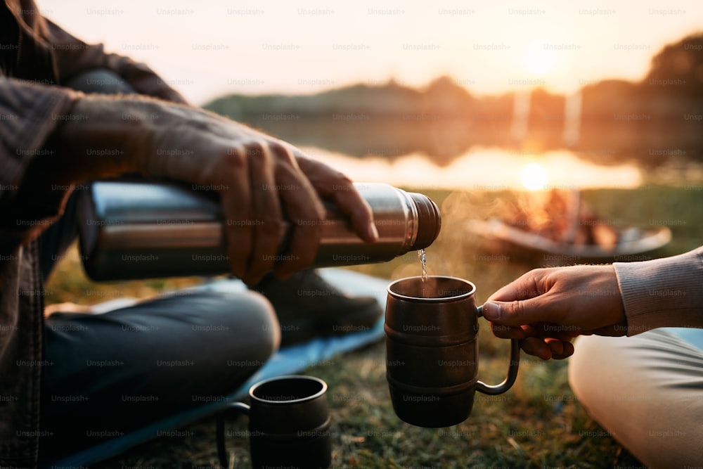 Nahaufnahme von Männern, die beim Angeln bei Sonnenuntergang ein heißes Getränk genießen.