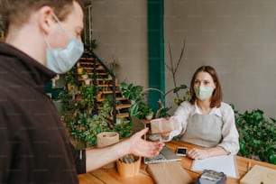 Mujer joven con máscara protectora que trabaja en una tienda que vende productos ecológicos de madera que le da una caja al cliente. Enfoque selectivo.