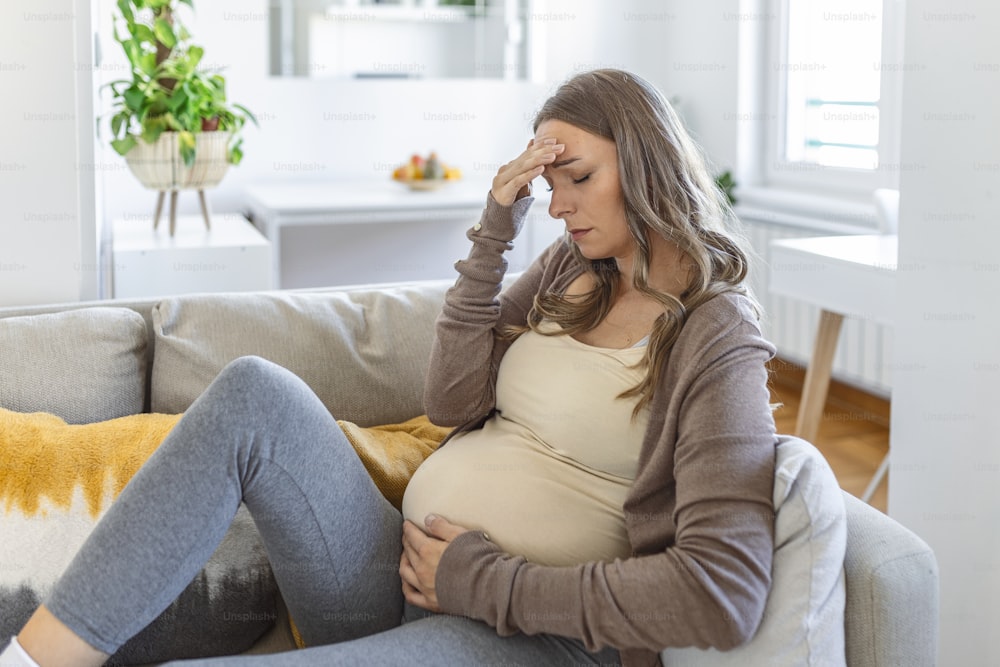 pregnant young adult woman resting on sofa at home, feeling unwell. Young pregnant woman has suffered from headaches sitting on the sofa. Pregnancy symptoms