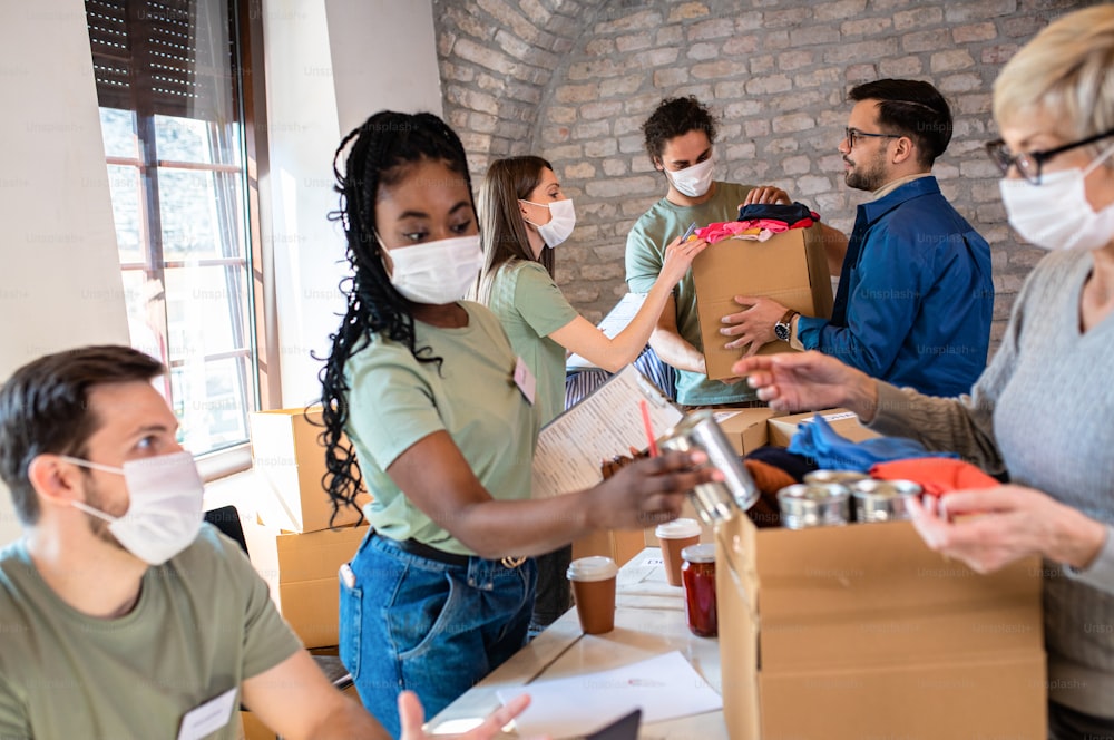 Group of volunteers with face mask working in community charity donation center.