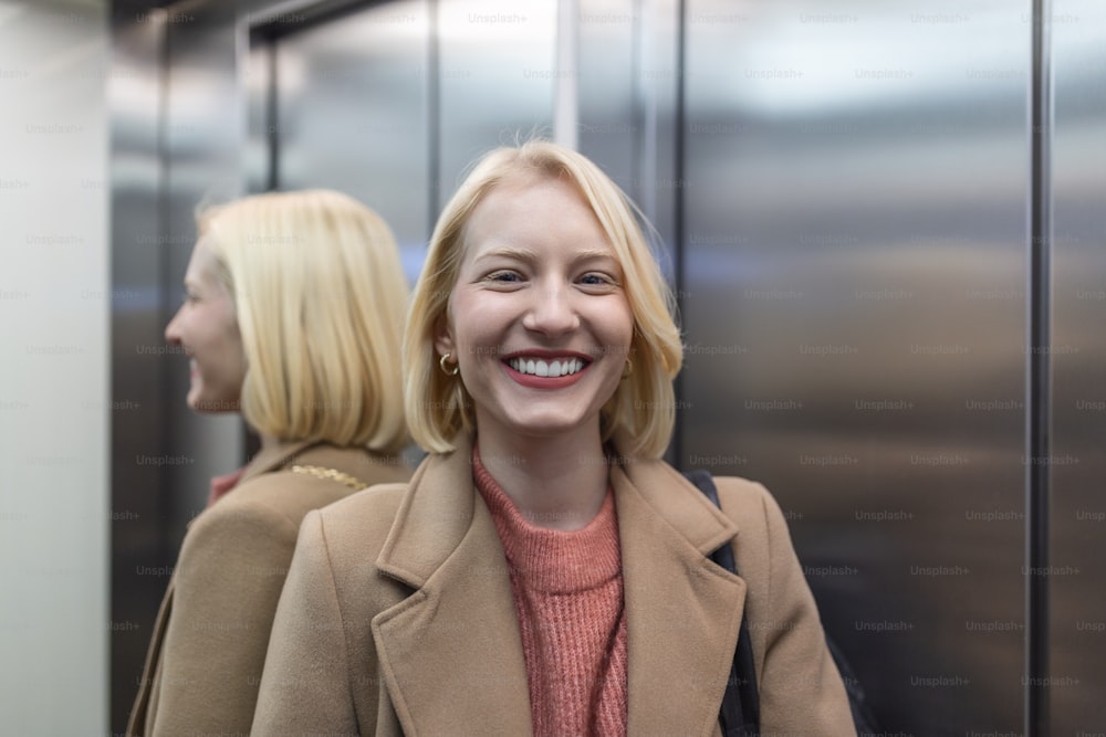 Cute blond female in trendy coat staying in lift alone and smiling, Woman in elevator