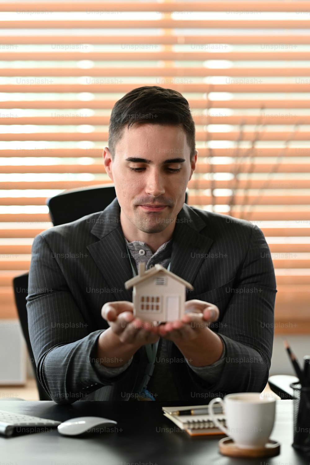 Portrait of attractive businessman holding house model. Mortgage and real estate investment concept.
