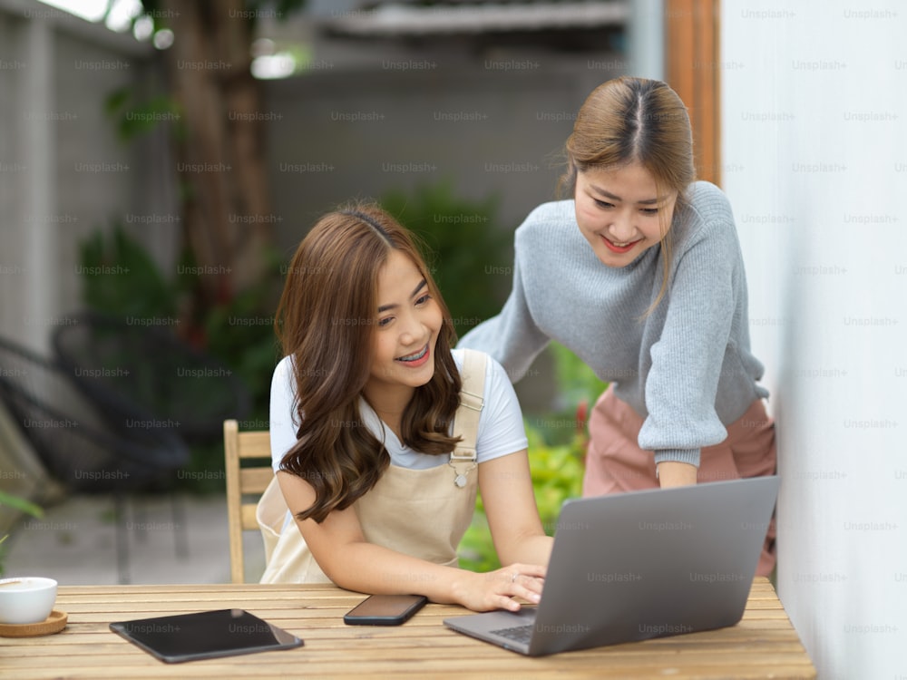 Two asian young female college students doing their assignment on laptop computer at backyard.