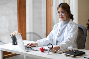 Médica especialista profissional sentada em sua mesa de escritório e trabalhando em seu laptop.