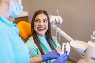 Pretty dentist doctor woman brushing jaw model at dental clinic, dental care concept. Dental care concept. Young woman dentist showing female patient jaw model at dental clinic