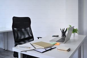 Interni per l'home office. Mockup computer portatile e forniture su tavolo bianco con comoda sedia da ufficio.