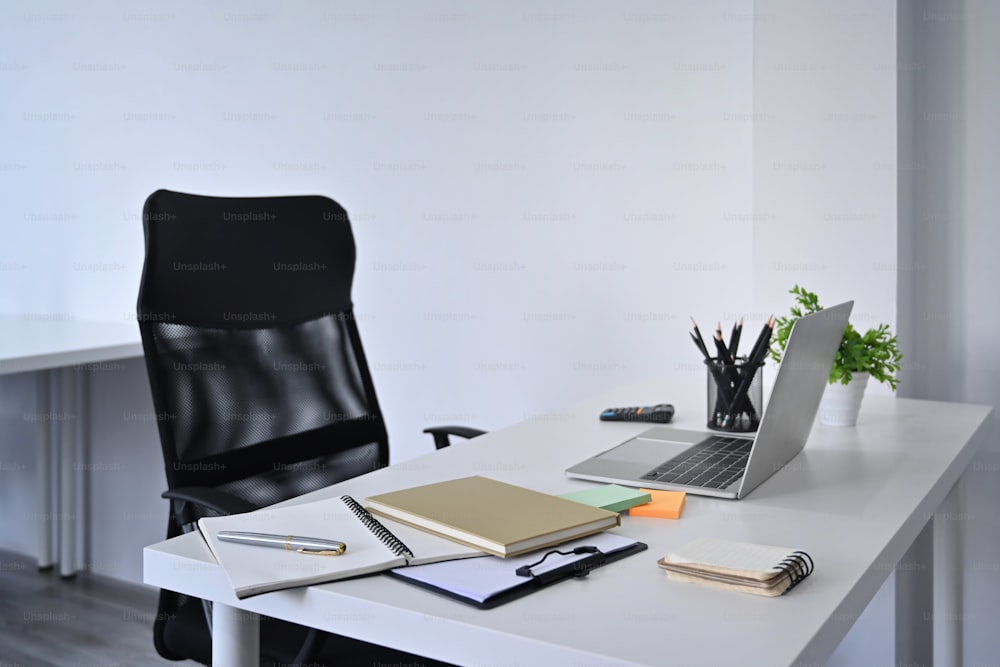 Home office interior. Mockup computer laptop and supplies on white table with comfortable office chair.