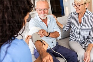 Krankenschwester spricht mit älteren Patienten während eines Hausbesuchs und misst den Blutdruck.