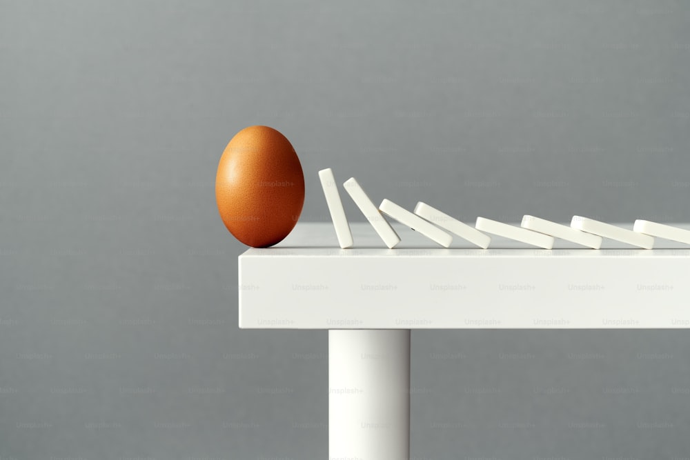 Uovo in equilibrio sul bordo di un tavolo, in procinto di cadere e rompersi a causa della caduta delle tessere del domino