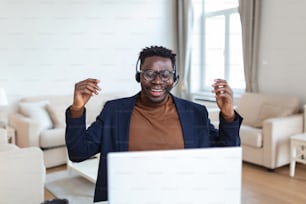 Hombre afroamericano emocionado con auriculares leyendo buenas noticias en el correo electrónico, obteniendo un nuevo trabajo, promoción, usando una computadora portátil, mirando la pantalla y gritando de alegría, mostrando un gesto de sí, celebrando