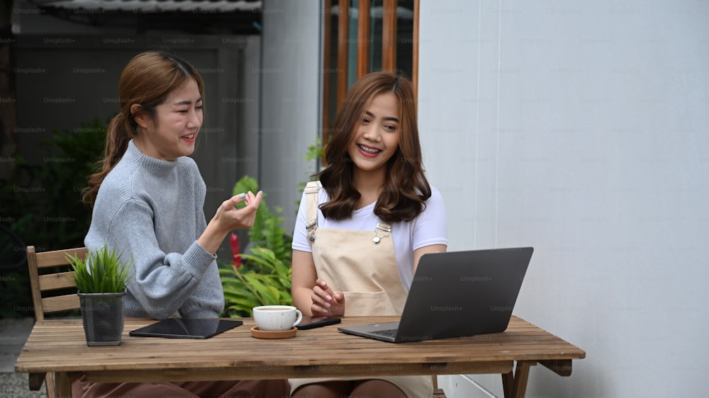 Dos alegres colegas de negocios trabajando juntos en una computadora portátil en un café al aire libre.