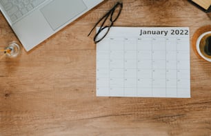 Top view of laptop and calendar of January 2022 on wooden background with blank space for text. Flat lay of workspace. Planning concept.