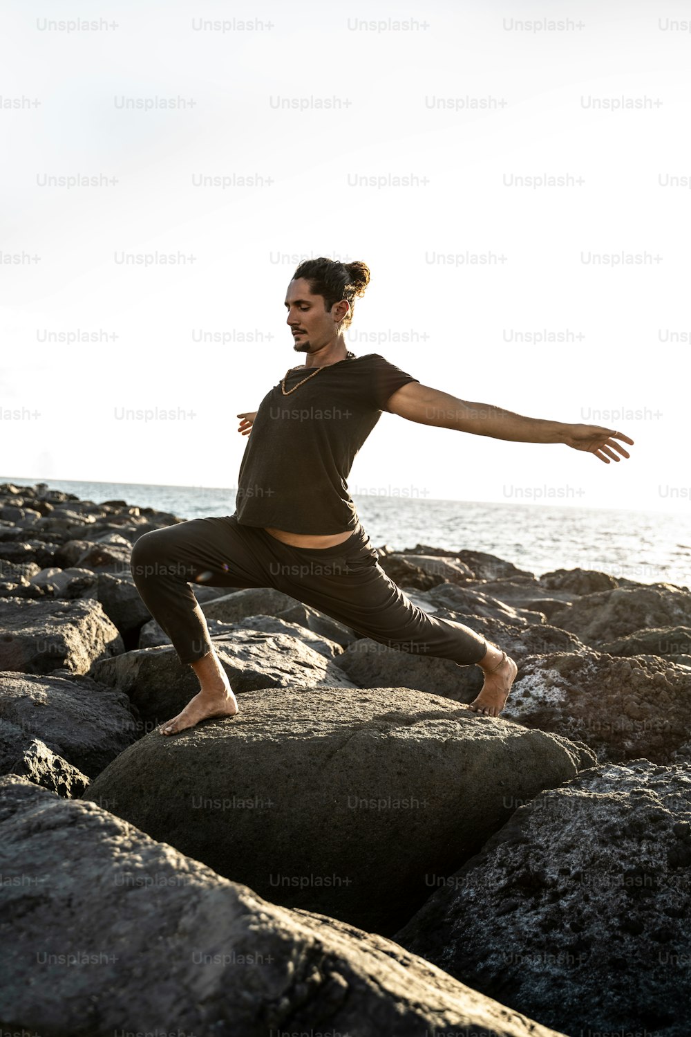 Un guapo profesor de yoga está practicando en las rocas, a la hora de la puesta del sol. Hombre haciendo ejercicio, estirando el cuerpo. Pranayama. Atención plena. Meditación.
