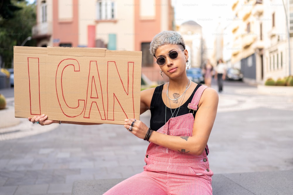 Girl power! Mulher jovem da moda segurando bandeira com palavras "eu posso". Olhar para a rua da cidade.