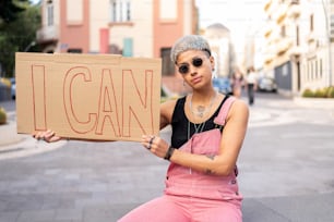Girl power! Young fashionable woman holding banner with "i can" words. City street look.