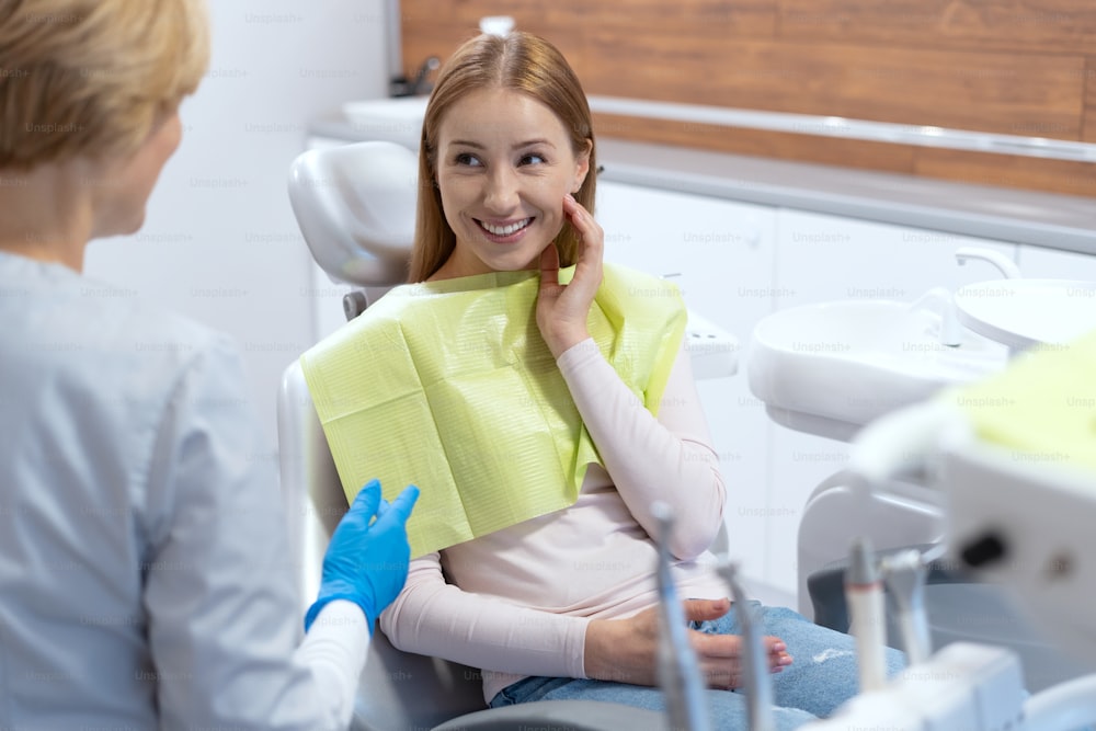 Ritratto di giovane donna sorridente che si sente felice dopo il trattamento dei denti. Consultazione con un professionista del settore. Moderno ambulatorio di stomatologia. Industria della medicina orale